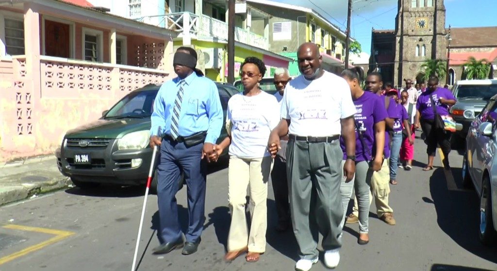 Minister Hamilton (blue attire), plays the role of blind man during an event dubbed ‘Walk a Mile in My Shoes', which was organised by the Association of Disabled Persons.
