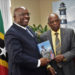 SIR KENNEDY SIMMONDS PRESENTS AUTOGRAPHED COPY OF HIS AUTOBIOGRAPHY TO PRIME MINISTER HARRIS